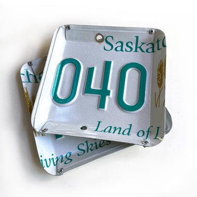 Square shaped catch all tray made from a recycled licence plate. Edges are bent and riveted together on corners to form a bowl shape.